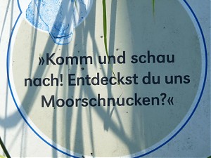 "Komm und schau nach! Entdeckst du uns Moorschnucken?" steht auf dem Schild. "Komm und schau nach! Entdeckst du uns Moorschnucken?" steht auf dem Schild.